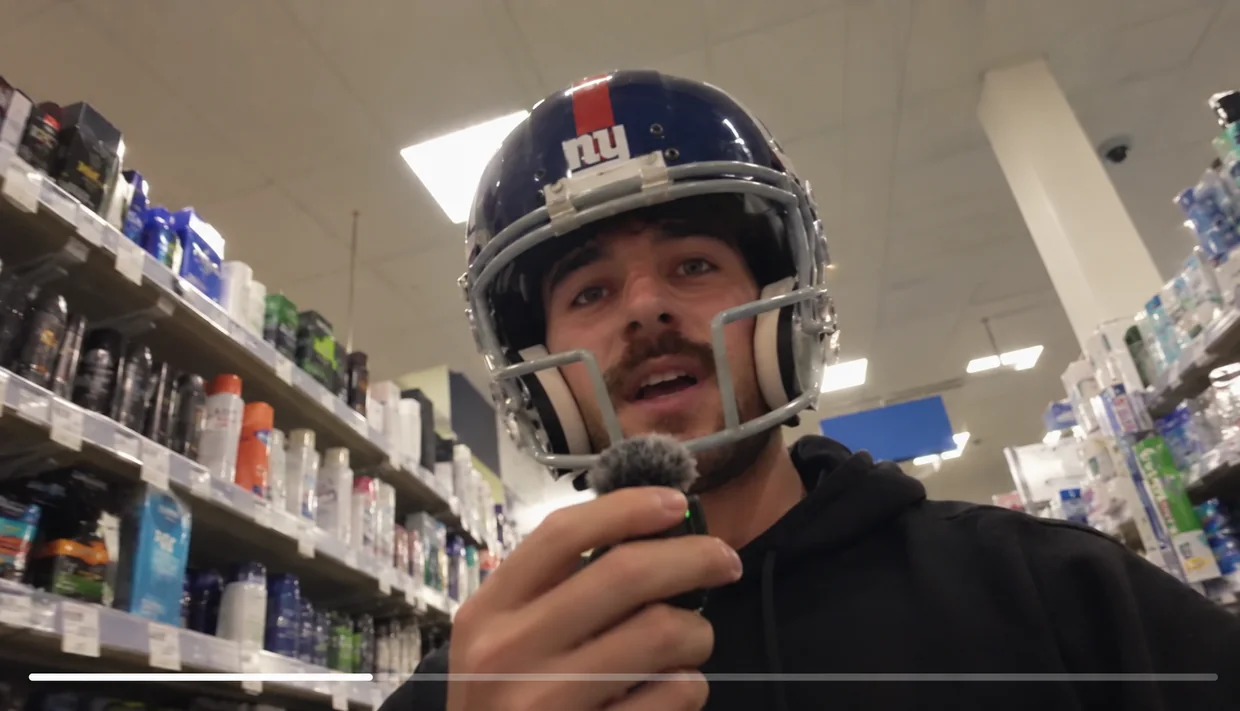 A man in a football helmet talking into a microphone in a drugstore aisle